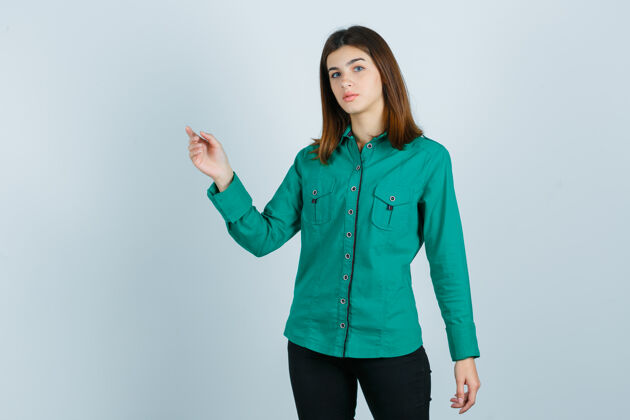 商业照片中的年轻女性穿着绿色衬衫 裤子 指着左上角看 眼前一片混乱指向问题困惑