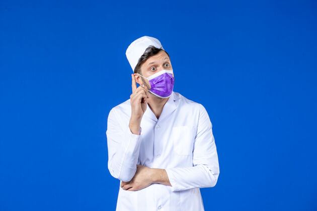 实验室外套前视图思考男医生在医疗服和紫色面具上的蓝色药物衣服外套