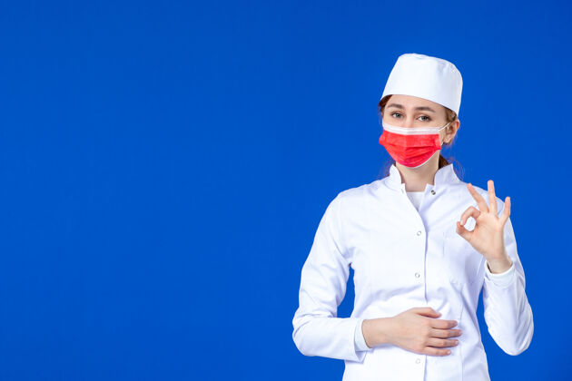 流行病身穿医疗服的年轻护士的正视图 蓝色的面具上有红色的面具病毒医院疾病