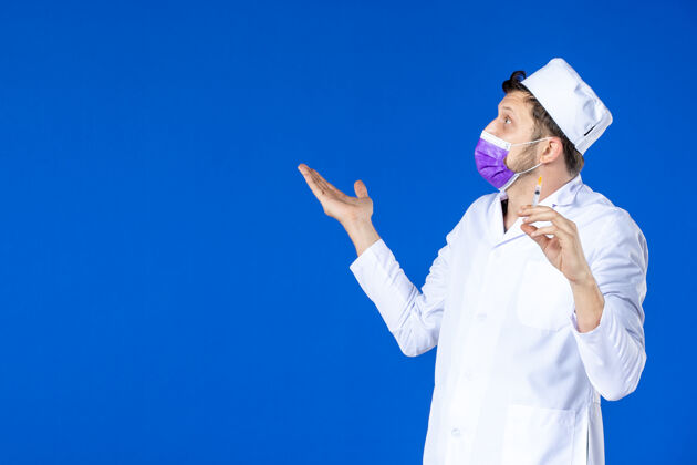 药品前视图中的男医生穿着医疗服和面具举行注射蓝色病毒治疗注射