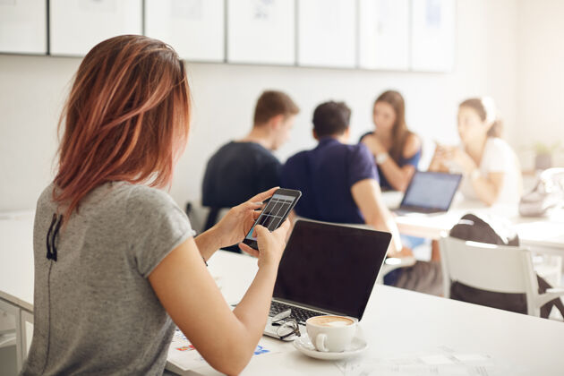 专业年轻的女商人在明亮的工作室或咖啡馆里用笔记本电脑和智能手机在线经营她的商店企业家的概念年轻室内女孩
