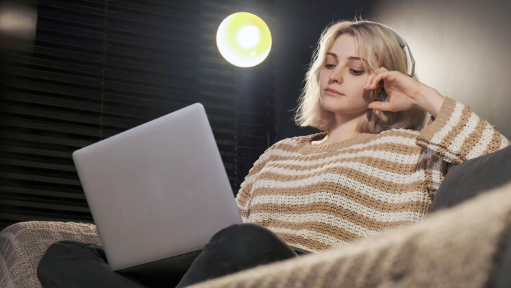 互联网一个戴着耳机的金发女孩坐在沙发上的笔记本电脑上科技笔记本电脑工作