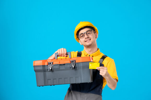 勤杂工身穿黄色制服的男工人正对着蓝色的工具箱盒子制服工具