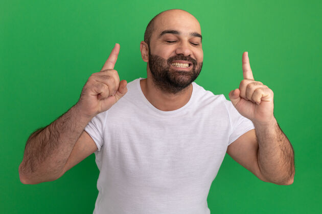 目录一个留着胡子的男人穿着白色t恤 开心地笑着 食指伸向绿色的墙壁男人胡子手指