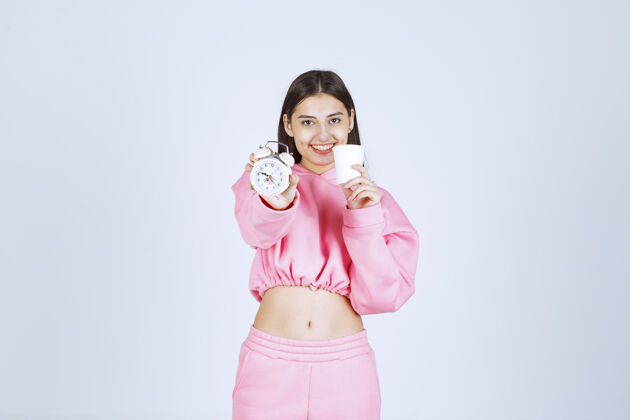 人体模特穿着粉色睡衣的女孩手里拿着闹钟和一杯咖啡年轻积极人