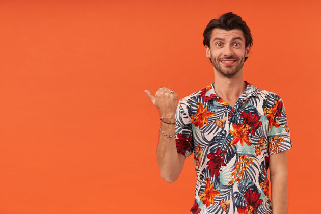 指向快乐迷人的年轻人 穿着夏威夷衬衫 用拇指指着广告空间的侧面镜头显示男人