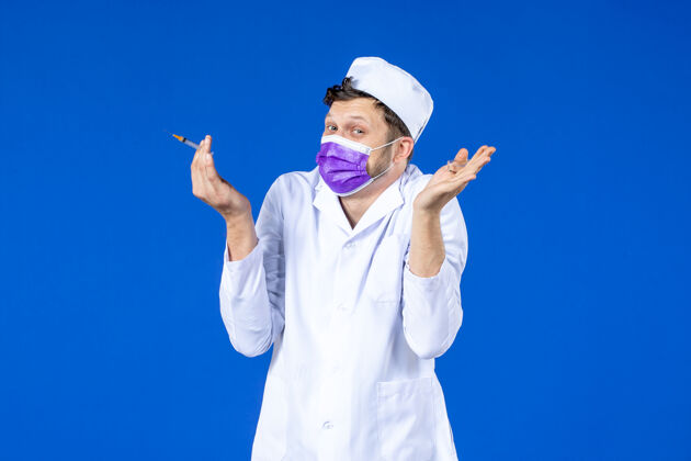 外套前视图中的男医生穿着医疗服和口罩持有疫苗和注射在蓝色注射药品病毒
