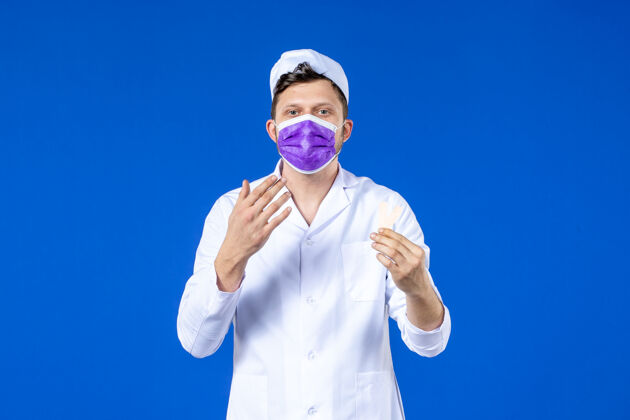 病毒前视图中的男医生穿着医疗服和面具举行小医疗补丁蓝色补丁衣服大流行