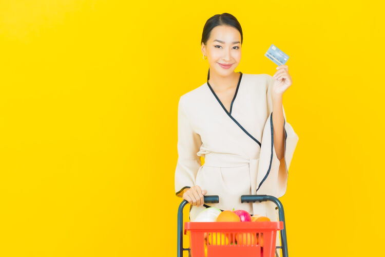 购买在黄色的墙上 一位年轻漂亮的亚洲女商人拿着购物篮在超市里买东西顾客消费者女性