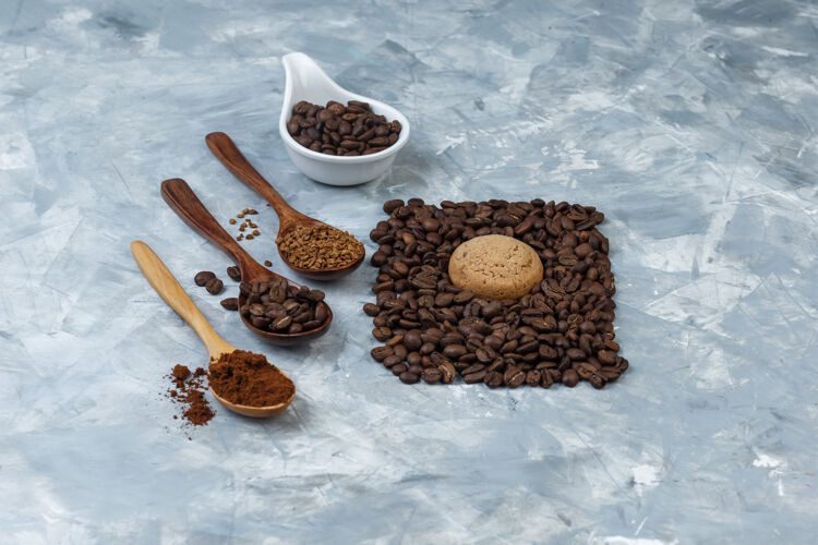 休息咖啡豆放在一个白色瓷壶里 用咖啡豆 速溶咖啡 咖啡粉放在木制勺子里 在浅蓝色大理石背景上高角度观看面粉早餐