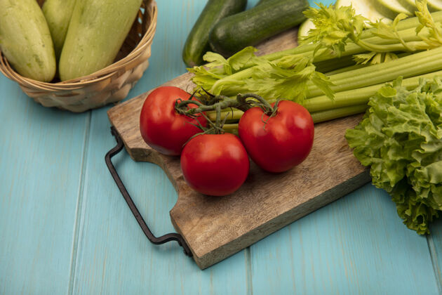 番茄顶视图新鲜芹菜上的木制厨房板与西红柿莴苣与西葫芦上的蓝色木制表面桶美味营养芹菜