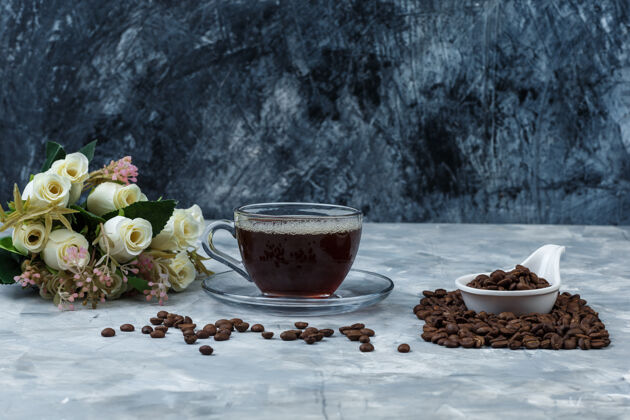 杯子把咖啡豆放在白瓷壶里 用一杯咖啡 花放在深蓝色和浅蓝色大理石背景上水平水壶花时间