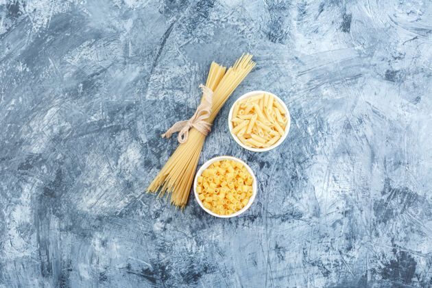 经典灰色灰泥背景上碗里的各种意大利面 顶视图罗勒传统烹饪