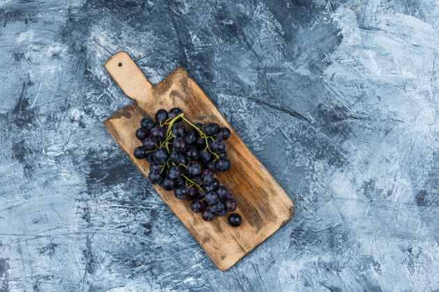 大平放在深蓝色大理石背景的砧板上的黑葡萄水平葡萄藤葡萄酒有机