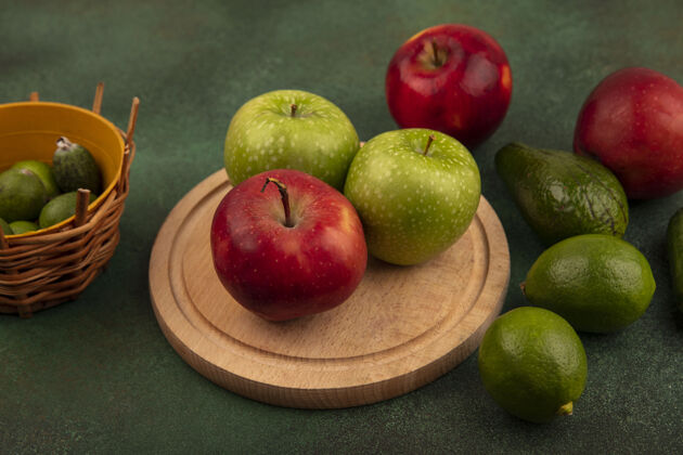 鳄梨木制菜板上美味的红苹果和绿苹果的俯视图 桶上放着酸橙和鳄梨 绿色的表面上孤立着美味木材中心
