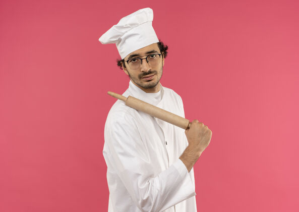 烹饪年轻的男厨师穿着厨师制服 戴着眼镜 肩上扛着擀面杖制服卷穿