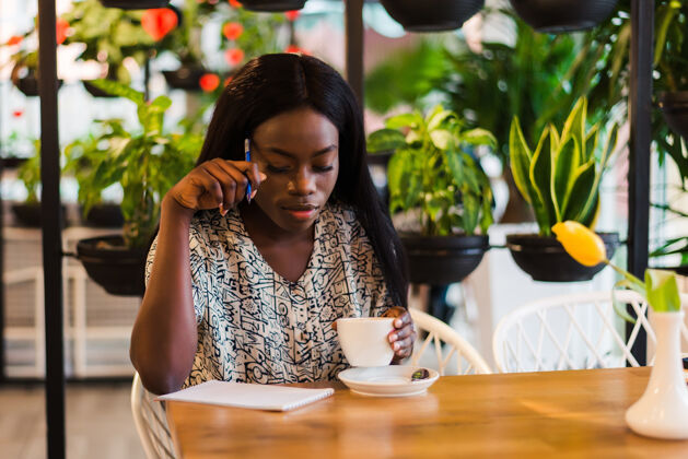 年轻人美丽的非洲女人在自助餐厅做笔记沉思食物桌子