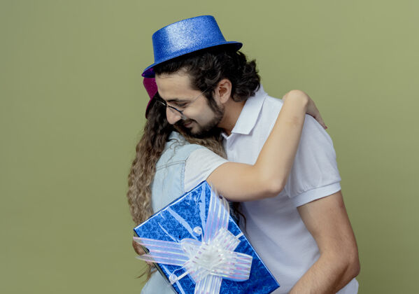 盒子高兴的年轻夫妇戴着粉红色和蓝色的帽子拥抱对方和家伙拿着礼品盒男人绿色帽子