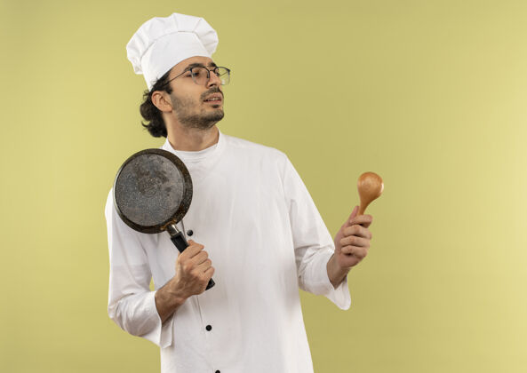 眼镜看着身边的年轻男厨师穿着厨师制服 戴着眼镜 手里拿着煎锅和勺子男制服厨师