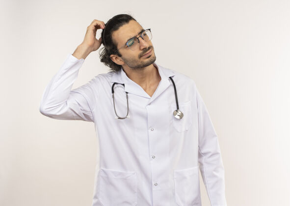 听诊器困惑的年轻男医生戴着眼镜 穿着白色长袍 手戴听诊器男性长袍医生