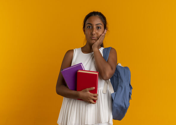 手关心的年轻女学生 背着书包 手放在脸颊上穿着橙色青少年
