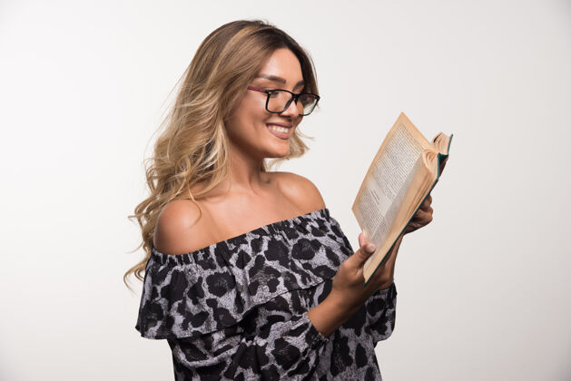 女人戴眼镜的年轻女子在白墙上看书年轻眼镜人