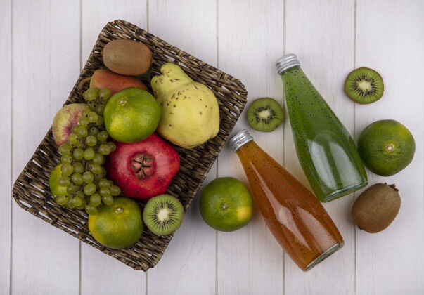 梨顶视果汁瓶与橘子石榴梨苹果葡萄和猕猴桃在一个篮子在一个白色的墙壁观点瓶子猕猴桃