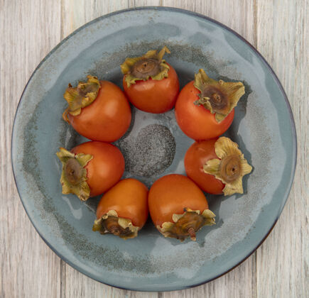 柿子在灰色木质表面的盘子上 可以看到柔软多汁的柿子的俯视图水果饮食新鲜