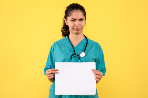 医院前视图困惑美丽的女医生穿着制服拿着文件站在黄色的背景上纸人抱