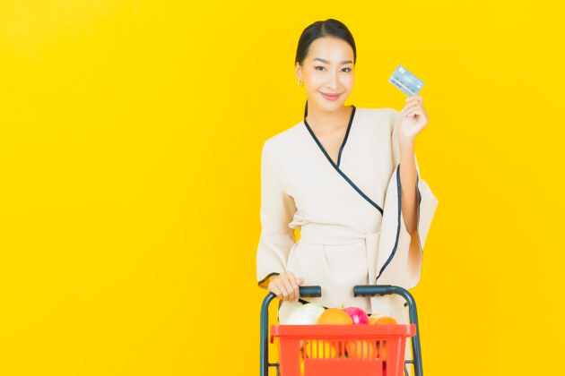 购买在黄色的墙上 一位年轻漂亮的亚洲女商人拿着购物篮在超市里买东西顾客消费者女性