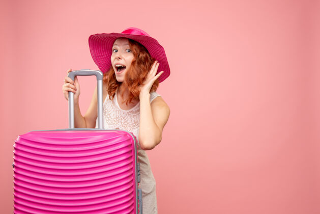 前面年轻的女性游客与粉红色的帽子和粉红色的墙壁上的包的正面视图肖像假期航行
