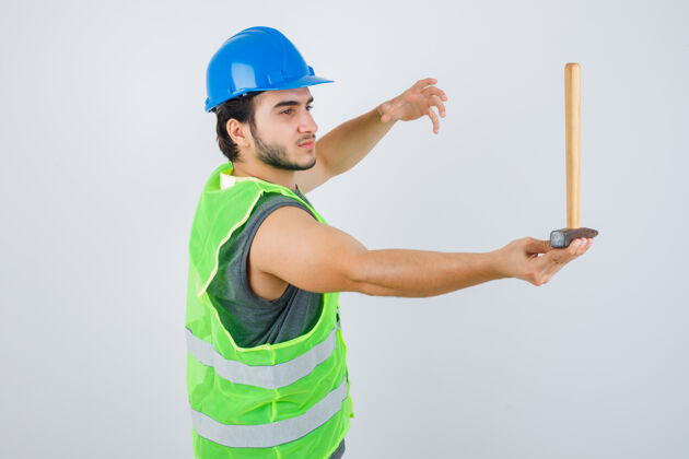 肖像年轻的建筑工人手里拿着锤子 手里举着工装制服 仔细地看着 正前方表情人建筑商