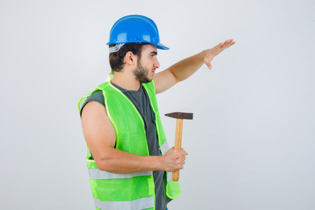 成人身穿工装的年轻建筑工人举起手 手持锤子 看上去自信满满 正面照建筑商人年轻