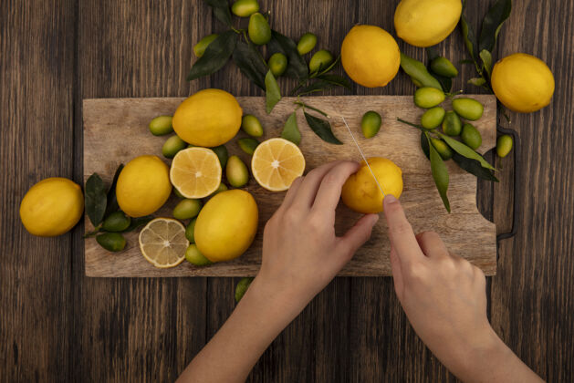 木材俯视图中的女性手切割新鲜的柠檬在一个木制的厨房板与刀与金坎隔离在一个木制表面女性饮食柑橘