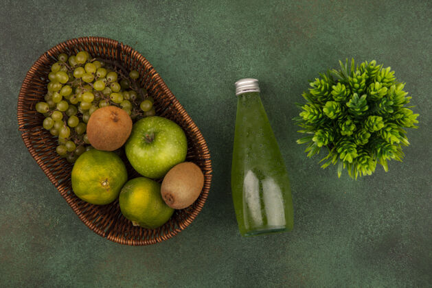 景观俯瞰绿色的橘子 绿色的墙上挂着一瓶果汁 篮子里放着苹果猕猴桃和葡萄苹果篮子果汁