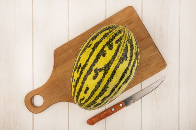 木材顶视图新鲜的哈密瓜在一个木制的厨房板上用刀在一个白色的木制表面夏天哈密瓜厨房