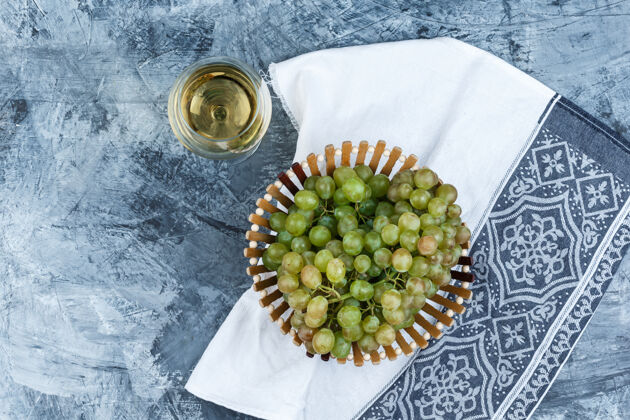 果汁一杯葡萄酒和绿色葡萄放在一个篮子里 背景是肮脏的石膏和厨房毛巾顶视图葡萄藤咕噜成熟