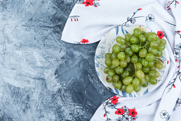 自然绿色的葡萄放在一个盘子里 背景是脏兮兮的石膏和厨房毛巾平铺食物多汁美味