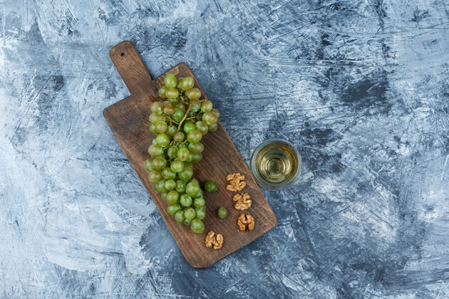 食物平放白葡萄 胡桃在砧板上 酒杯放在深蓝色大理石背景上水平葡萄多汁的生的
