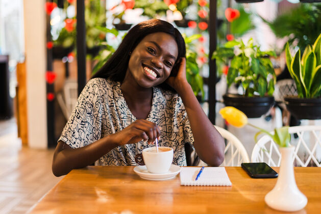 人在咖啡馆喝咖啡的快乐的年轻黑人妇女的特写肖像卷发非洲美丽