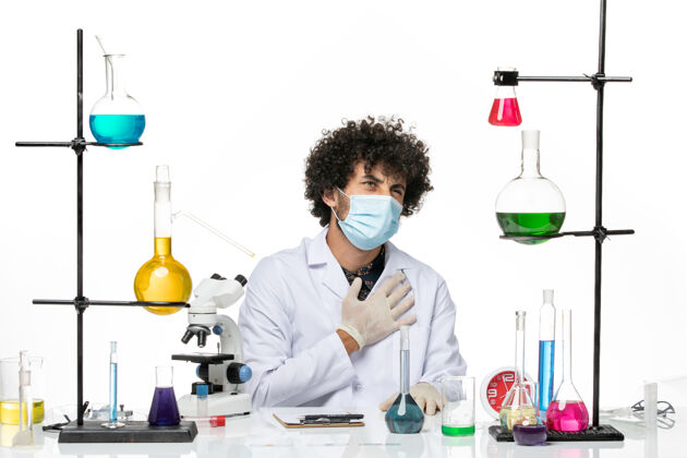 医院前视图男性化学家穿着医疗服 戴着面罩 坐在一个浅白色的空间里 拿着溶液男性化学家医学坐姿
