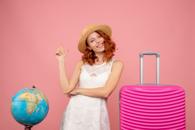 头发年轻女性游客的正面图 粉红色的墙上挂着粉红色的包美丽夏天衣服