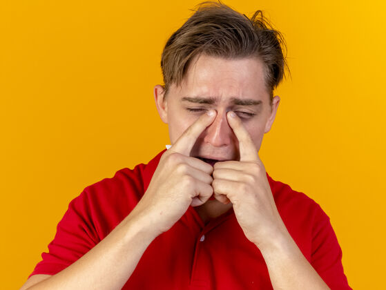 特写特写镜头：悲伤的年轻英俊的金发病患在橙色的墙上闭着眼睛触摸鼻子男人手势疾病