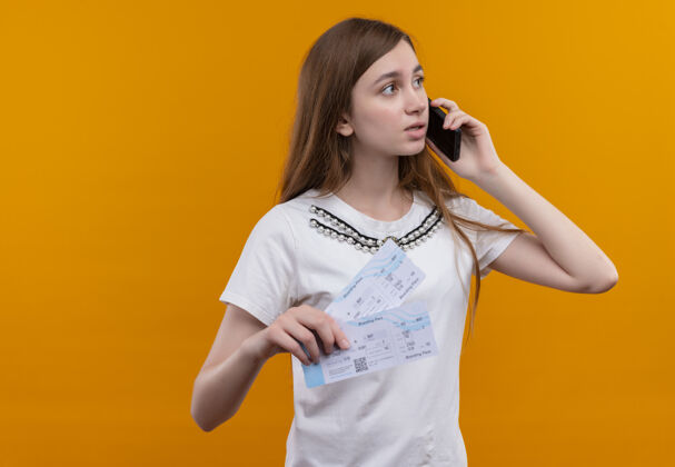 女人年轻的旅行女孩在电话里聊天 手里拿着机票 看着右侧隔离的橙色墙壁上的复印空间侧线手持电话