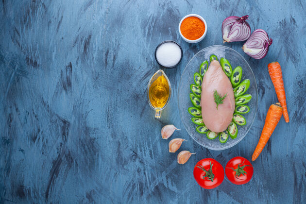 番茄把鸡胸肉和辣椒片放在玻璃盘子里 旁边放着香料 油和各种蔬菜 放在蓝色的上面鸡配料玻璃盘