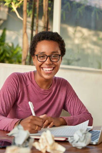 工作场所开朗微笑的黑人大学生在写课程论文穿孔计算机记者