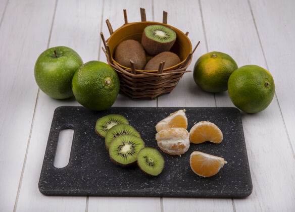 橘子前视图切菜板上的橘子片 篮子里有猕猴桃 白墙上有绿橘子和苹果篮子板前面