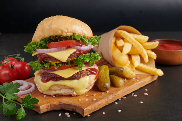 美味自制汉堡包或汉堡配新鲜蔬菜 奶酪生菜和蛋黄酱 炸薯条放在黑石桌上的牛皮纸上快餐和垃圾食品的概念美味烧烤芝麻