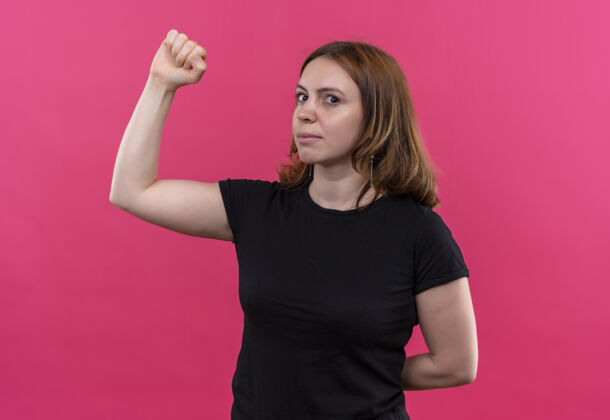 姿态年轻随意的女人在孤零零的粉色墙上做着坚强的手势年轻女人强壮
