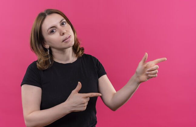 随意年轻随意的女人在孤立的粉红色墙上指着右边年轻侧身右指